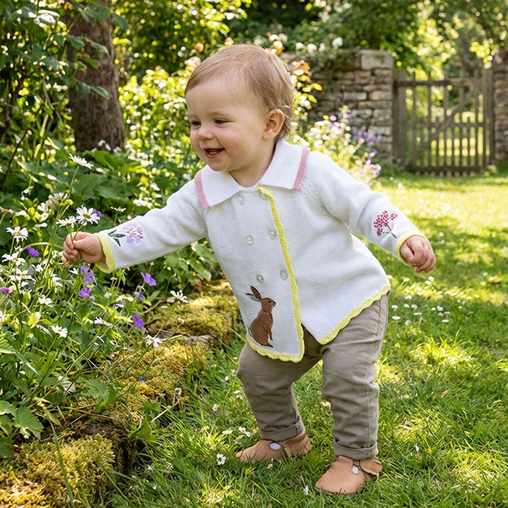 Baby wearing Meadow Knitted Pram Coat in a garden