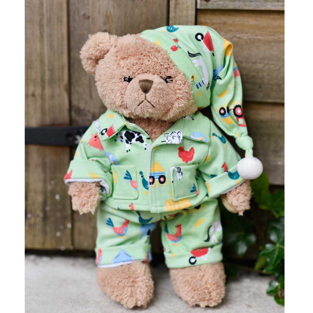 Teddy bear wearing mint green farmyard print pyjamas and nightcap sitting against a wooden fence