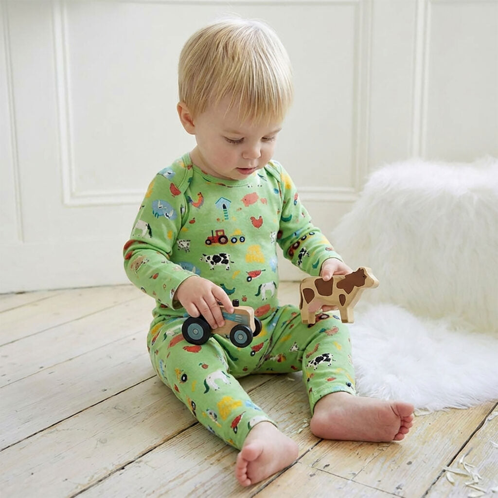 Baby wearing Farmyard Print Jumpsuit sitting on a wooden floor playing with toy tractor and cow