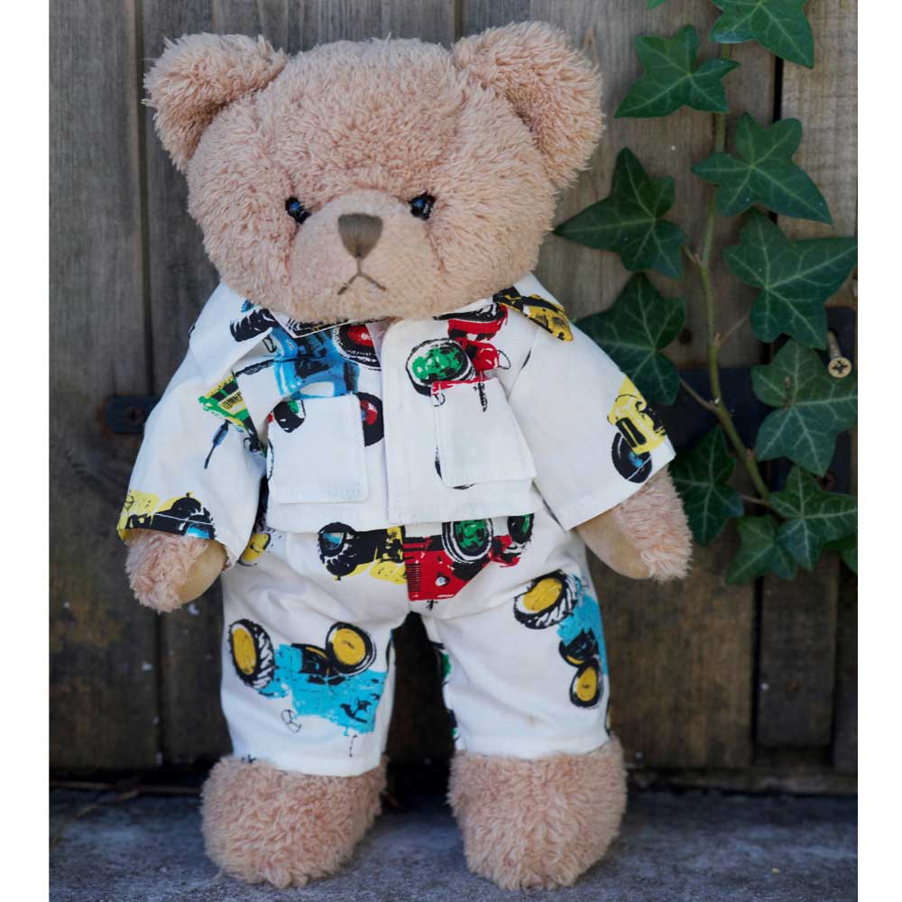 Teddy bear wearing tractor print pyjamas standing against a wooden fence with ivy