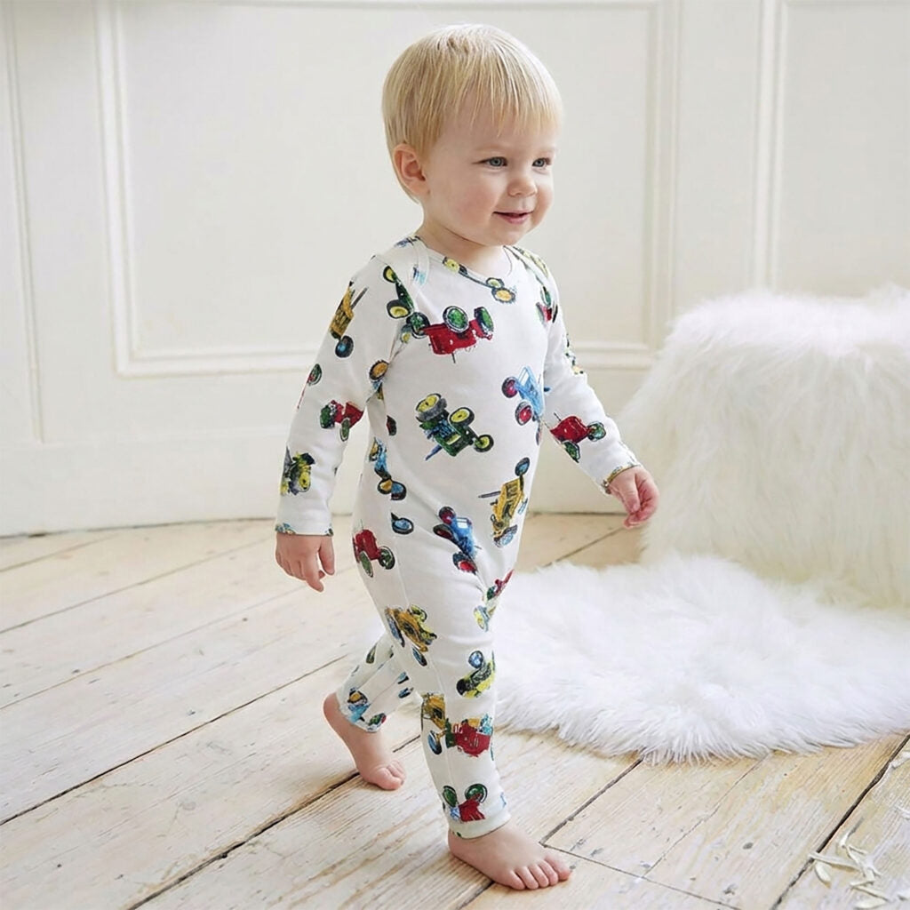 Baby toddler wearing white tractor print jumpsuit walking on wooden floor