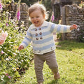 Baby toddler wearing blue and cream striped sheep pram coat with wooden buttons, running through a cottage garden