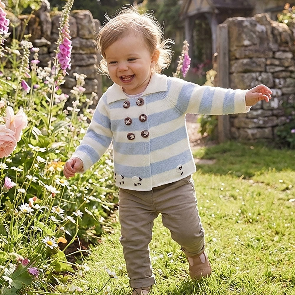 Baby toddler wearing blue and cream striped sheep pram coat with wooden buttons, running through a cottage garden